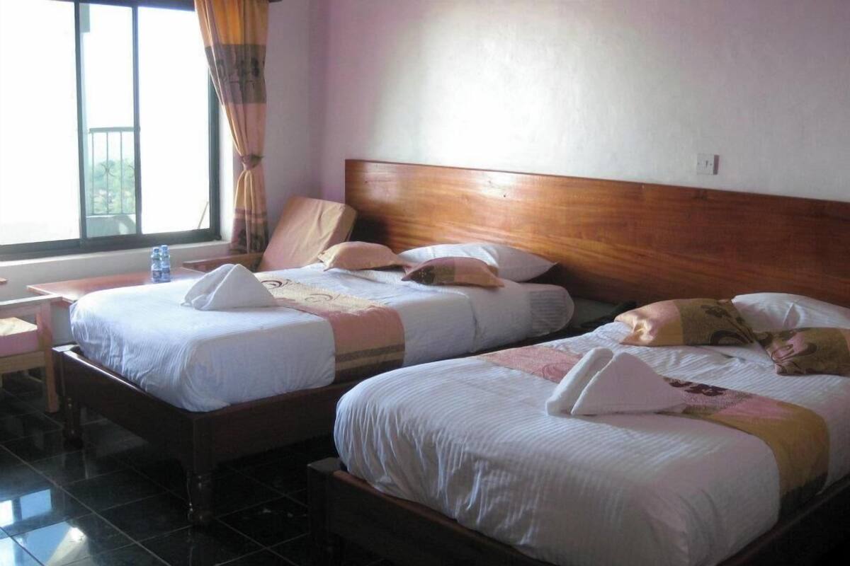Habitación de hotel con dos camas, cabecero de madera, ventana con cortinas y piso de baldosas.