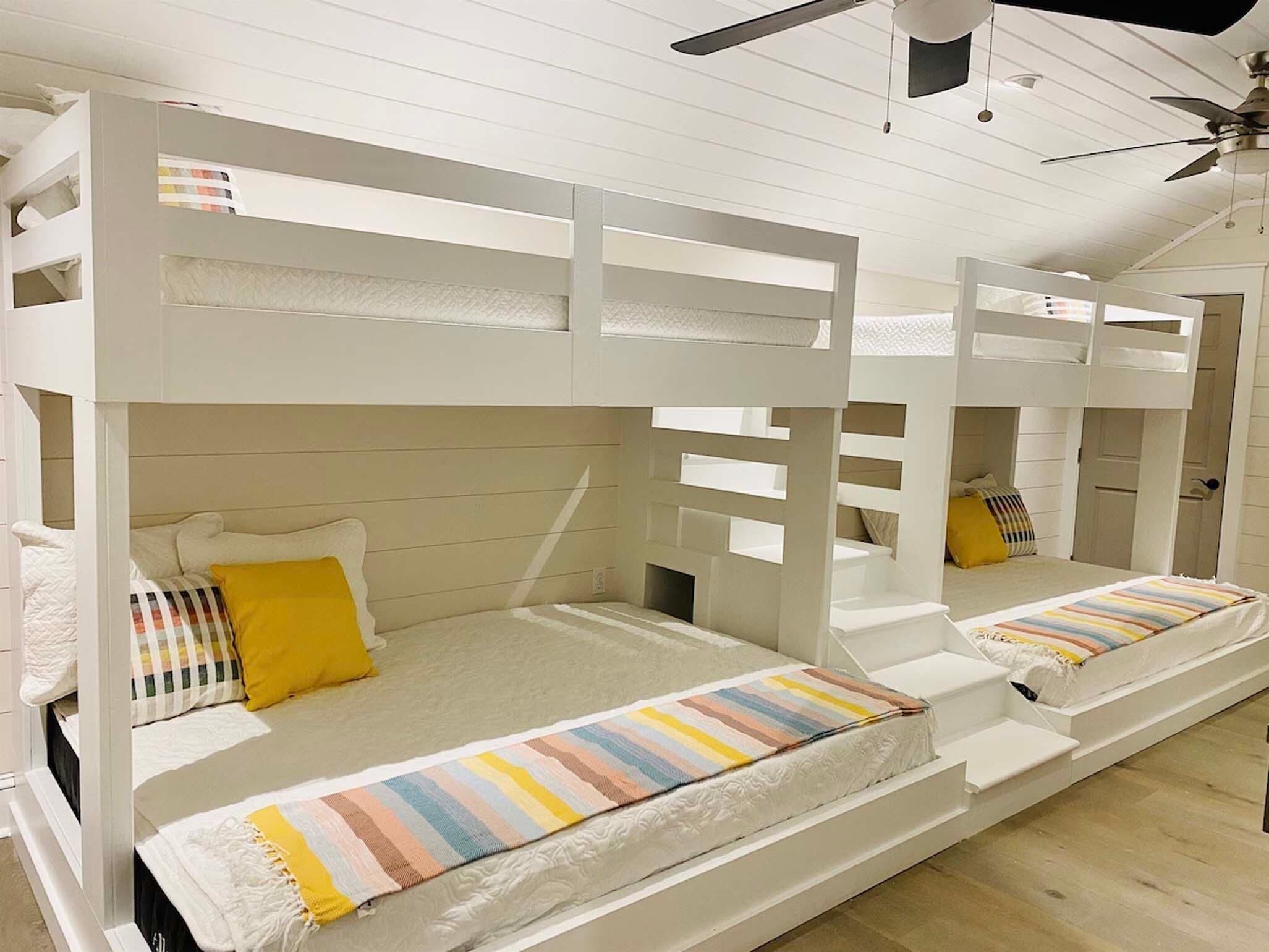 A bunk bed room with white railings and a striped blanket on the lower bunk.