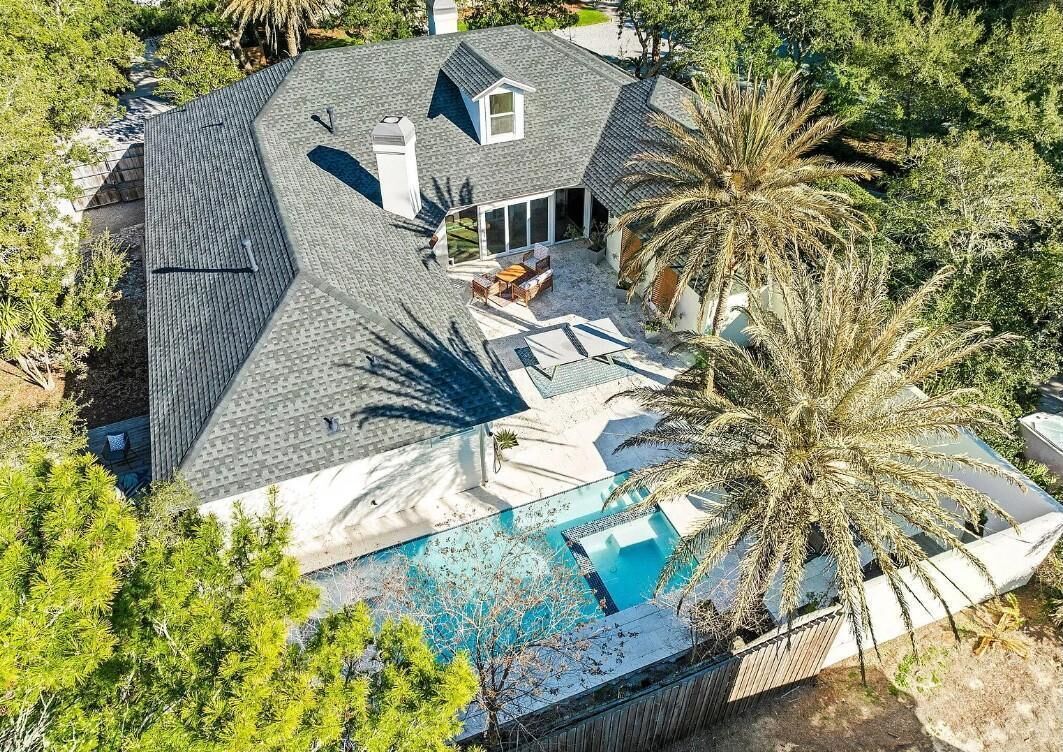 An aerial view of a house with a large swimming pool, a covered patio, and a landscaped yard with palm trees.