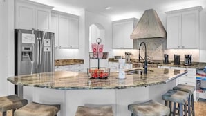 A modern kitchen with a central island, white cabinetry, stainless steel appliances, and a built-in range hood. - Saltaire (Santa Rosa Beach)