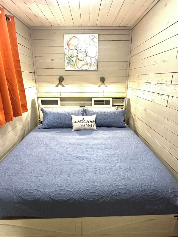 A bedroom with a bed, two wall-mounted lamps, a painting, and a 'welcome home' pillow. - Container Home with Rooftop Deck, Amazing Views, Full Kitchen and Bath, Wi-Fi (French lick)