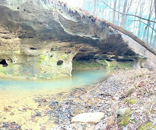 Formación rocosa natural con una entrada similar a una cueva y una pequeña poza de agua.