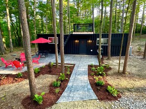 A modern outdoor patio with a stone pathway, red chairs, and a dining area with a red umbrella. - Container Home with Rooftop Deck, Amazing Views, Full Kitchen and Bath, Wi-Fi (French lick)