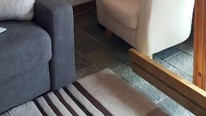 Ein gemütliches Zimmer mit einer Holzwand, einem grauen Sofa, einem weißen Sessel und einer Stehlampe.