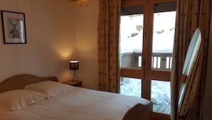 Ein Schlafzimmer mit einem Bett, einer Nachttischlampe, einem gerahmten Bild und einem Fenster mit Vorhängen.