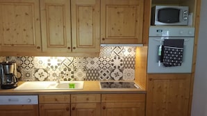 Eine Küche mit Holzschränken, einer Mikrowelle, einem Backofen, einer Kaffeemaschine und einer gemusterten Spritzschutzwand.
