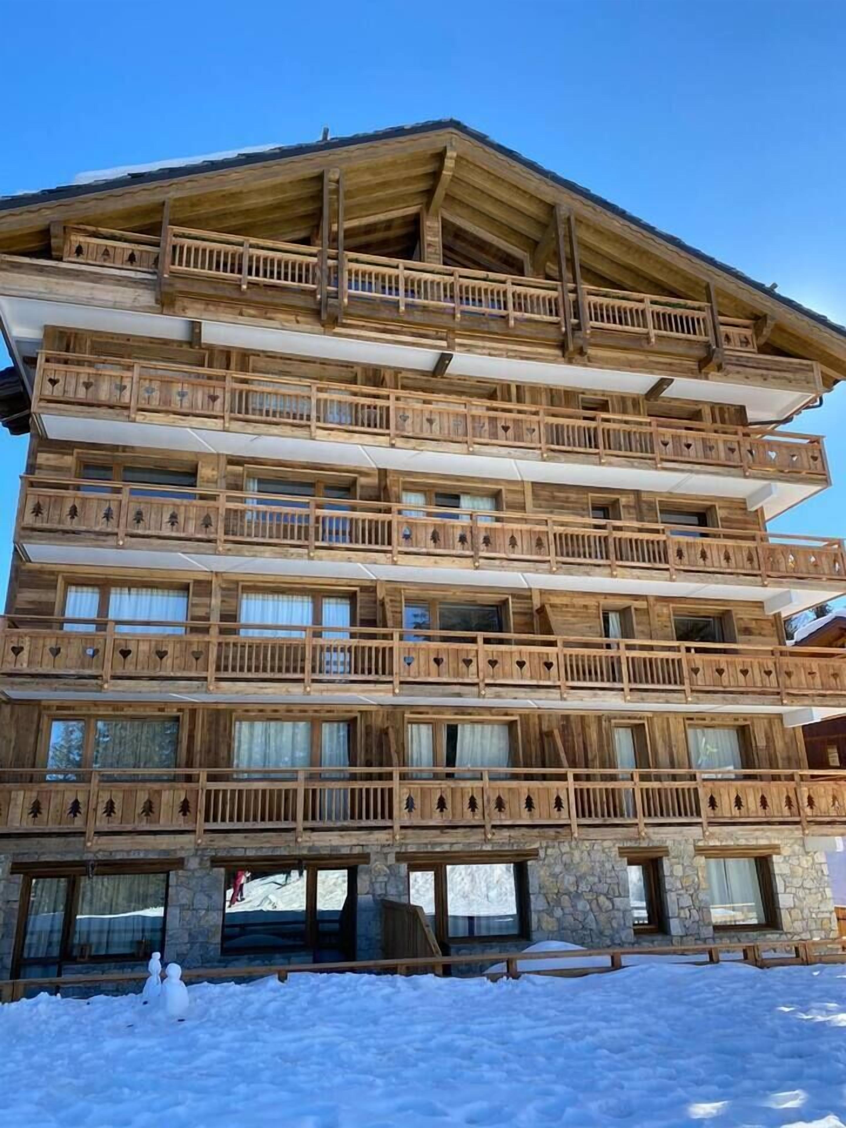 Een meerlaags houten gebouw met balkons, een stenen fundering en grote ramen.