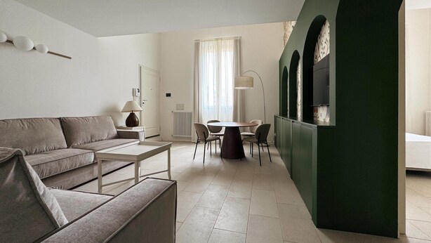 A modern living room with a sofa, a coffee table, a dining table with chairs, and a green accent wall. - Charme & design three-room (Bologna)