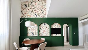 A dining area with a round wooden table and four chairs, a green accent wall with floral wallpaper, and a modern pendant light. - Charme & design three-room (Bologna)