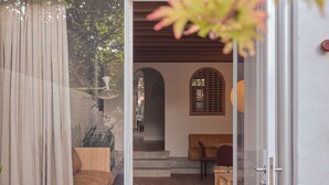 A room with a wooden bench, a small table, and a view of a garden through a glass door.
