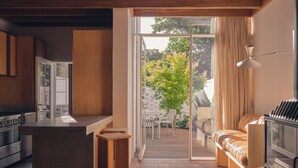 A modern kitchen with a central island, a dining area with a sofa and table, and a sliding glass door leading to an outdoor patio with a wooden deck and chairs.
