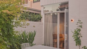 A modern outdoor seating area with a table and chairs, a glass door leading to a room, and a white brick wall.
