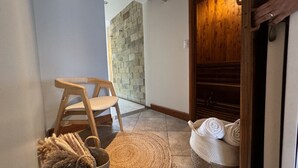 A room with a stone wall, a wooden door, a wooden chair, a woven rug, and a basket with towels. - Spacious 5BR in Escazu w/Jacuzzi, Sauna & Fire Pit (San Rafael)