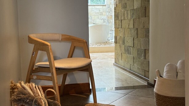 A wooden chair in a room with a stone wall and a view of a bathtub. - Spacious 5BR in Escazu w/Jacuzzi, Sauna & Fire Pit (San Rafael)