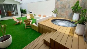 A backyard with a hot tub, wooden deck, green artificial turf, and outdoor furniture. - Spacious 5BR in Escazu w/Jacuzzi, Sauna & Fire Pit (San Rafael)