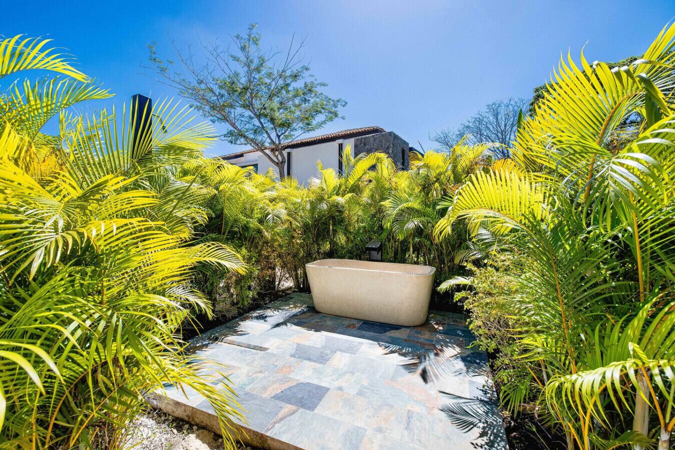 Une terrasse en pierre avec un espace salon extérieur de couleur beige, entouré d’une végétation tropicale luxuriante.