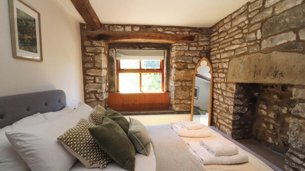 A bedroom with a stone wall, a bed with pillows, a window, and a fireplace. - Sunnybrook Cottage (Lancaster)