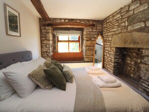 Ein Schlafzimmer mit Steinwand, einem Bett mit Kissen, einem Fenster und einem Kamin.