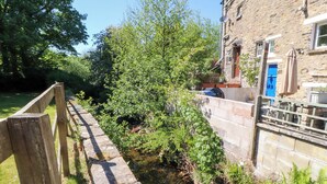 A narrow waterway with a wooden bridge, stone walls, and lush greenery. - Sunnybrook Cottage (Lancaster)