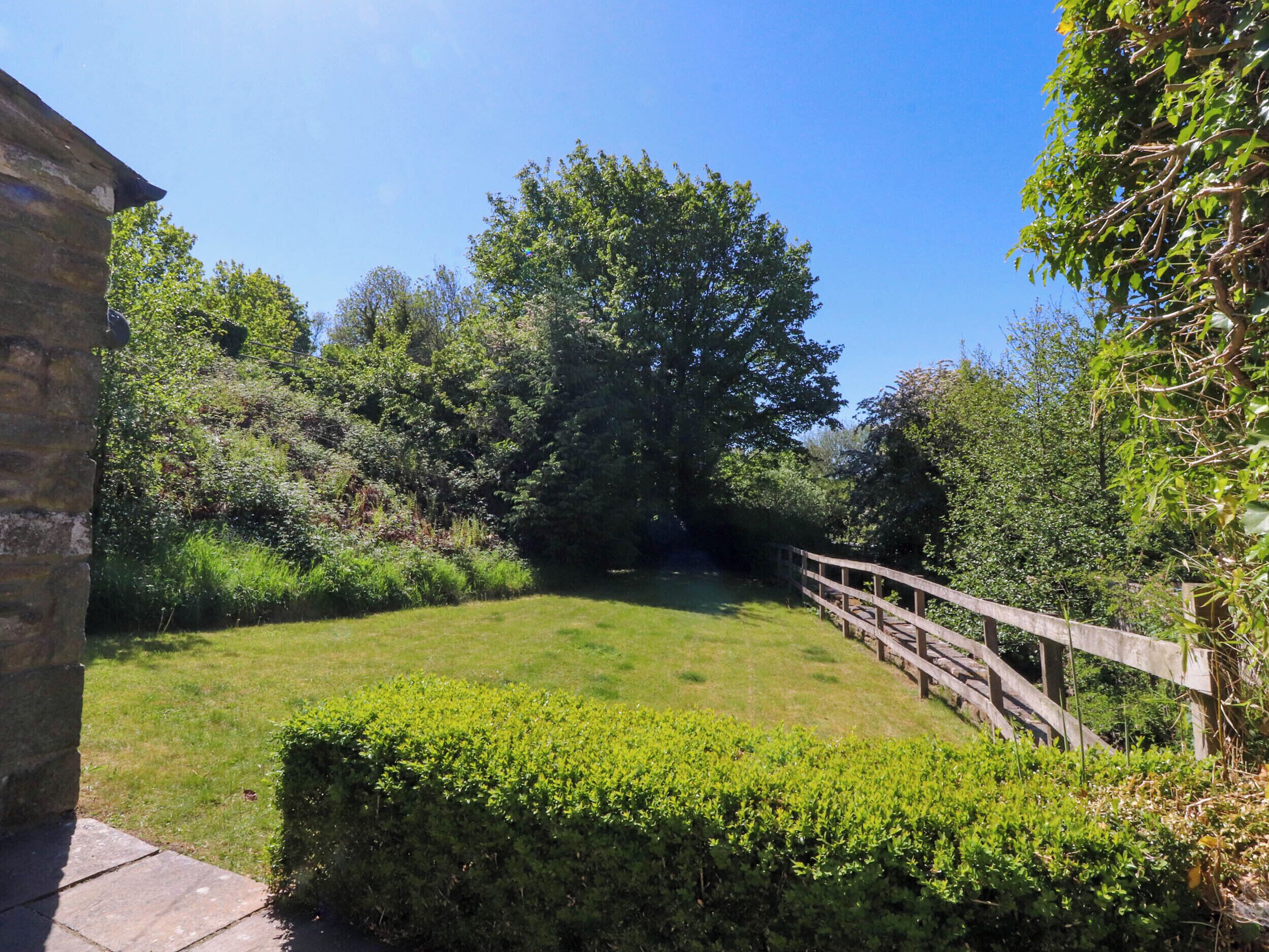 A grassy courtyard with a wooden bridge, surrounded by dense foliage and trees.