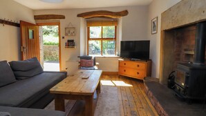 A cozy living room with a sofa, a wooden table, a television, and a fireplace. - Sunnybrook Cottage (Lancaster)