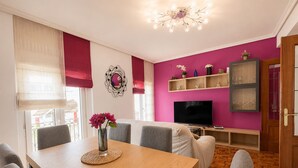 A room with a dining table, chairs, a TV, a bookshelf, and a door. - Charming apartment in Castro (Castro-Urdiales)