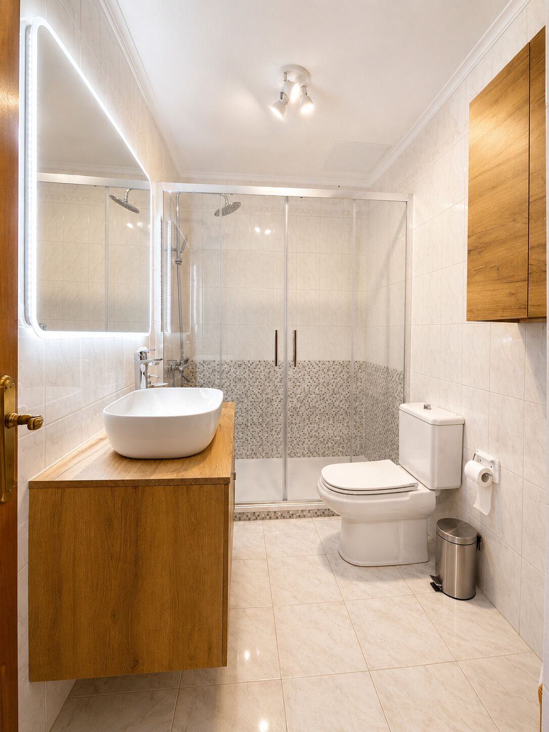 Et moderne badeværelse med en brusekabine i glas, en hvid vask og et toilet.