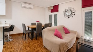 A room with a dining table, chairs, a sofa, a glass coffee table, an air conditioning unit, and a decorative mirror. - Charming apartment in Castro (Castro-Urdiales)