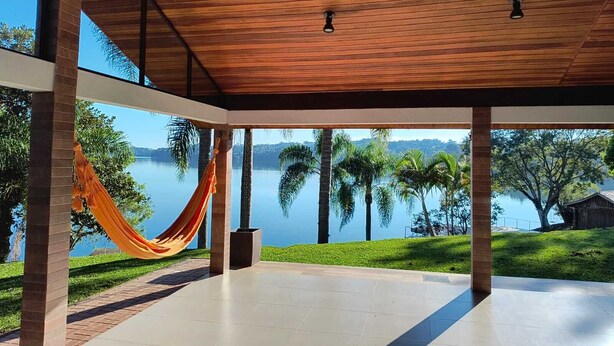 Un amplio patio cubierto con vista a un lago tranquilo y palmeras.