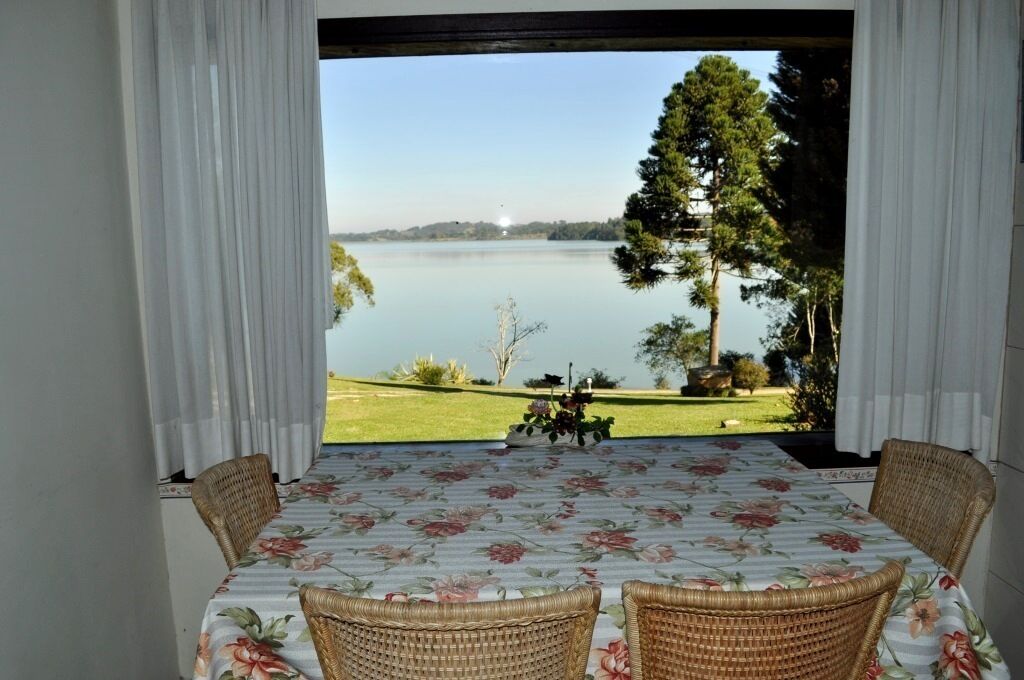 Un coin repas avec une table dressée pour deux personnes, donnant sur un lac bordé d’une étendue herbeuse et de quelques arbres.