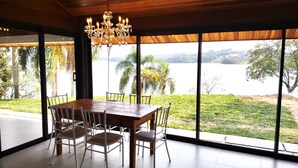Comedor con mesa y sillas de madera, ventanas amplias con vista a un lago y follaje.