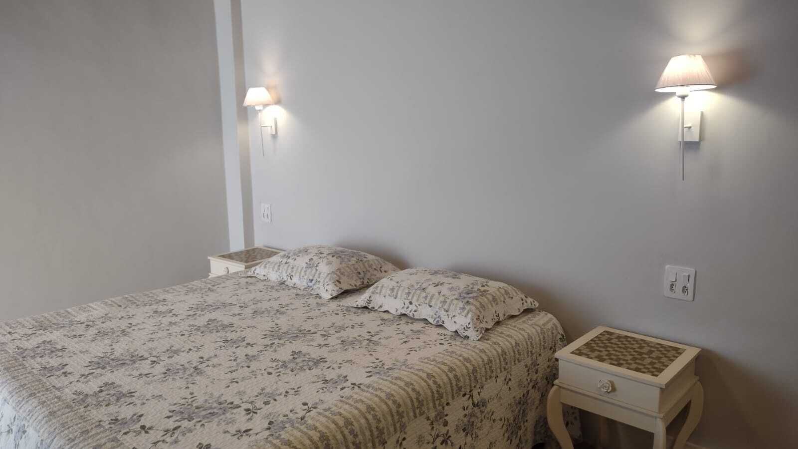 Une chambre à coucher avec un lit, deux lampes fixées au mur et une table de chevet sur laquelle se trouve un jeu d’échecs.