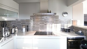 A modern kitchen with white cabinets, a stainless steel range hood, and a tiled backsplash. - Apartment in Het Zoute With Sea Views (Knokke-Heist)