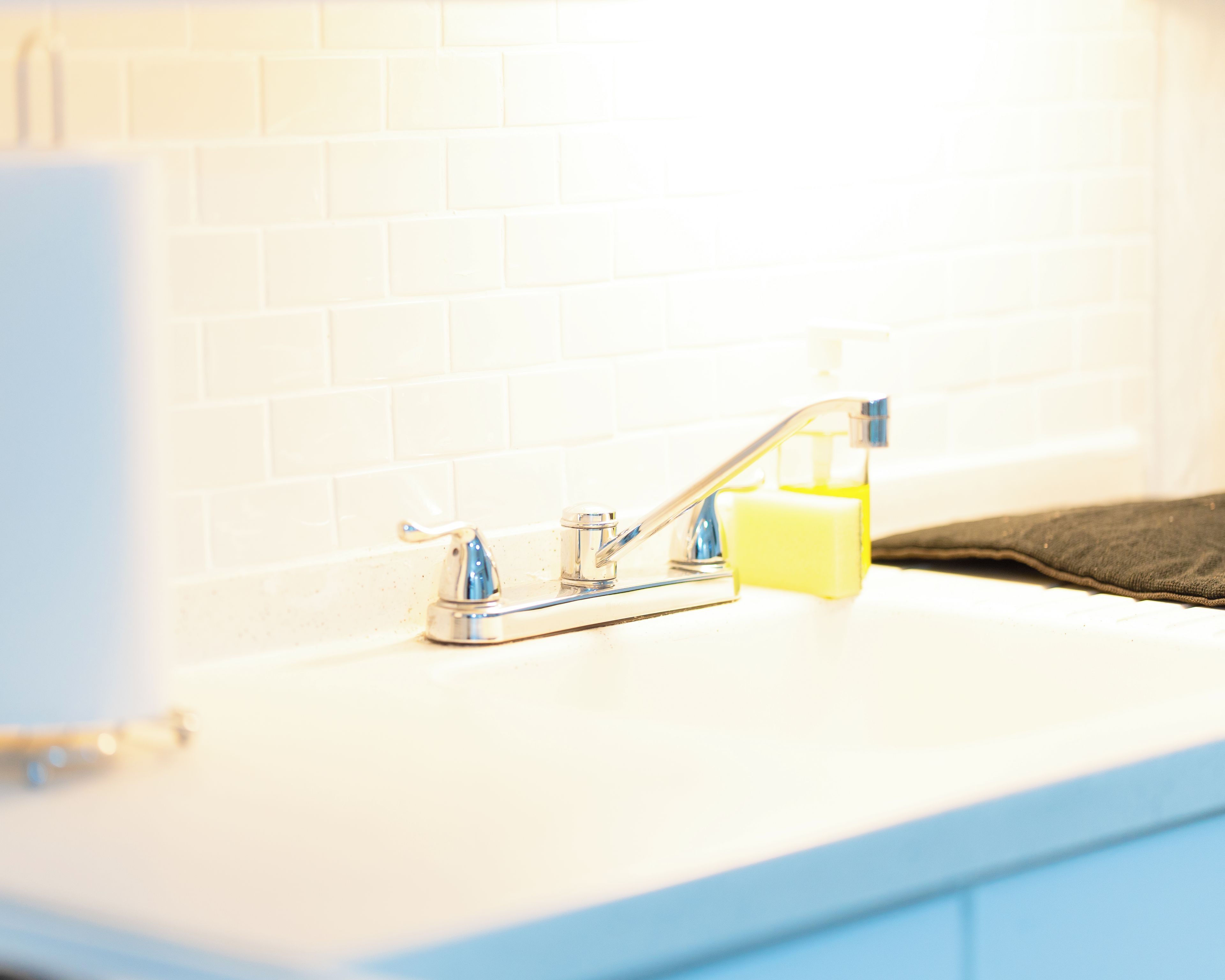 A bathroom with a white tiled wall, a chrome faucet, and a soap dispenser on the counter.