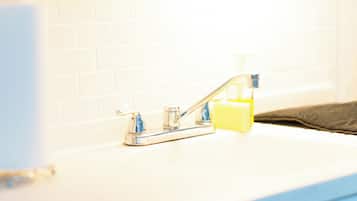 A bathroom with a white tiled wall, a chrome faucet, and a soap dispenser on the counter.