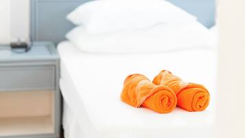 Una cama bien hecha con sábanas blancas y dos toallas naranjas enrolladas sobre la cama.