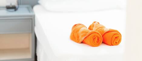 A neatly made bed with white sheets and two rolled orange towels placed on the bed.