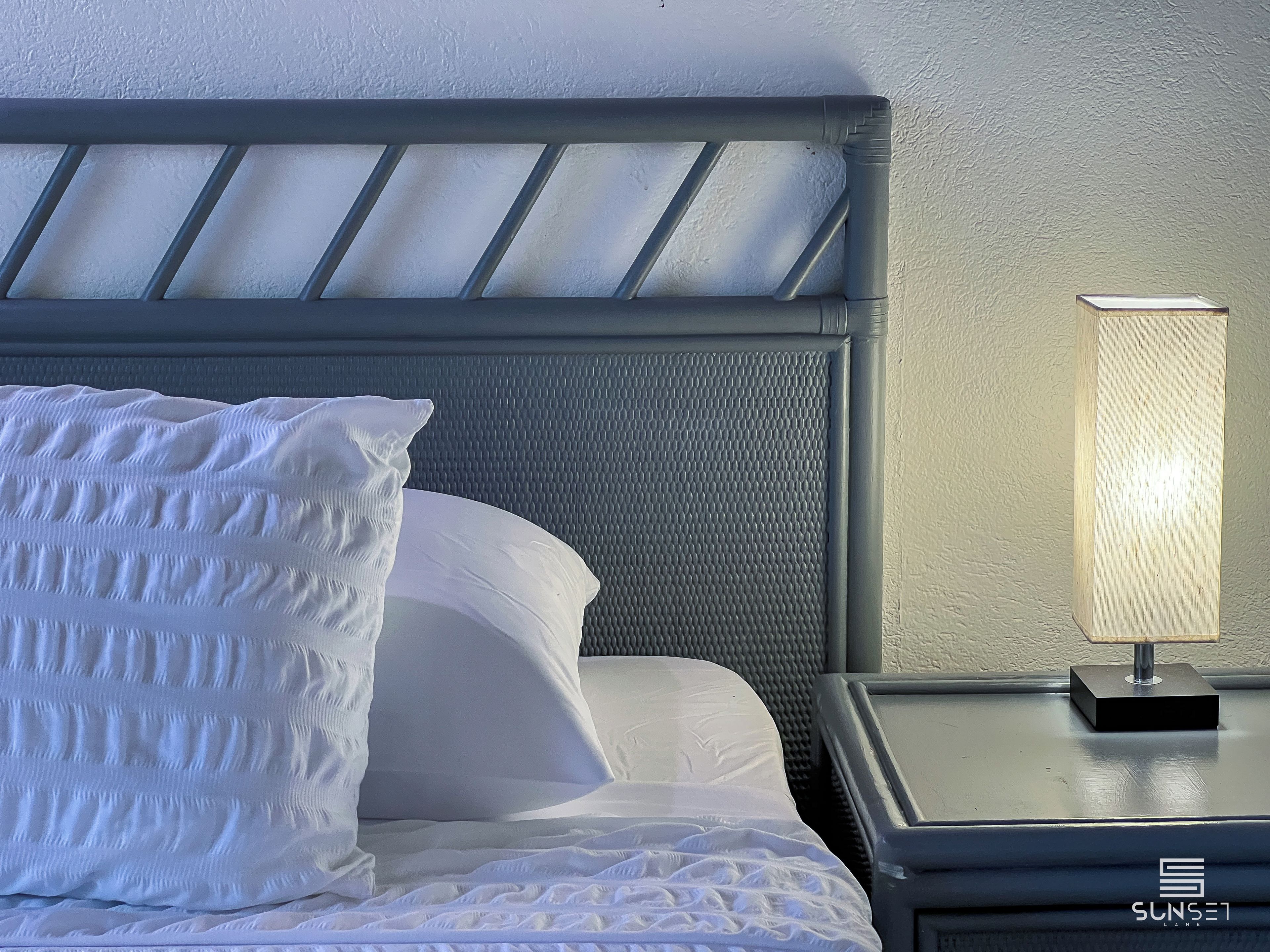 A neatly made bed with a headboard, a bedside lamp, and a textured wall.