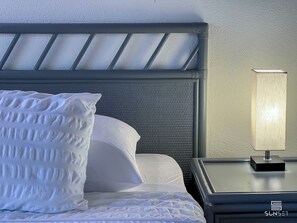 A neatly made bed with a headboard, a bedside lamp, and a textured wall. - Sunset Lane Apartment Hotel (Holetown)