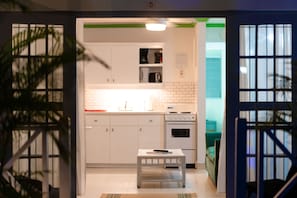 A modern kitchen with white cabinets, a built-in oven, and a small table with a remote control. - Sunset Lane Apartment Hotel (Holetown)