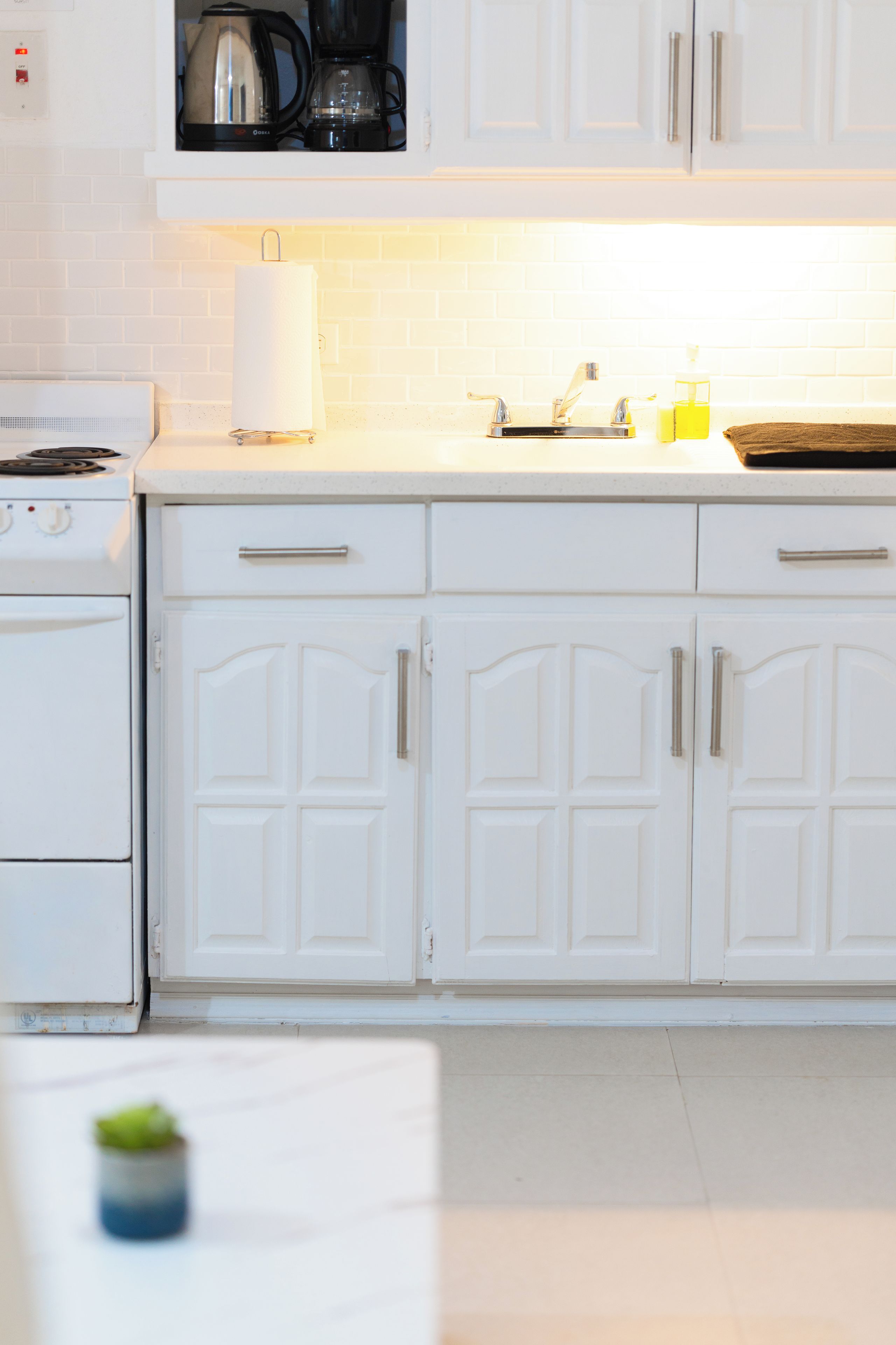 Una cocina con armarios blancos, estufa, fregadero y cafetera.