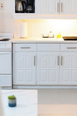 Une cuisine avec des meubles blancs, une cuisinière, un évier et une machine à café.