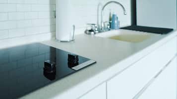 A modern kitchen with a white countertop, a black induction cooktop, a stainless steel sink, and white cabinets.