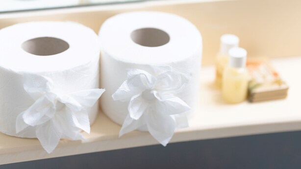 Deux rouleaux de papier toilette décorés de nœuds, un petit flacon et une boîte posés sur une surface en bois.