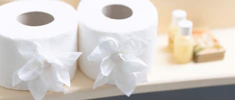 Two rolls of toilet paper with bows, a small bottle, and a box on a wooden surface.