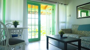 Une pièce avec une porte verte, des murs blancs, un canapé à motifs, une chaise blanche et une table sur laquelle est posée une plante.