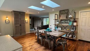 A dining area with a wooden table and chairs, a kitchen with a built-in oven, and a skylight above the dining table. - Careys Refuge - Family Retreat with Huge Fenced Yard (Bothell)