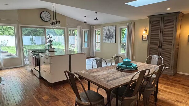 A spacious kitchen with a central island, large windows, and a dining area with a wooden table and chairs. - Careys Refuge - Family Retreat with Huge Fenced Yard (Bothell)