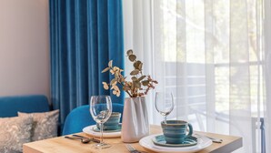 Ein Esstisch mit blauen Keramiktellern, einer weißen Vase mit grünen Blättern und zwei Weingläsern.