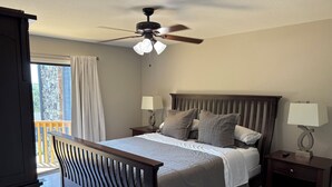 Un dormitorio con cama, dos mesitas de noche, ventilador de techo y vistas al exterior.
